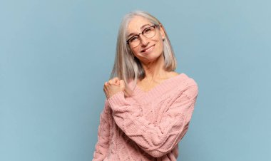 Orta yaşlı bir kadın mutlu, pozitif ve başarılı hissediyor, bir meydan okumayla karşılaştığında motive oluyor veya iyi sonuçları kutluyor.