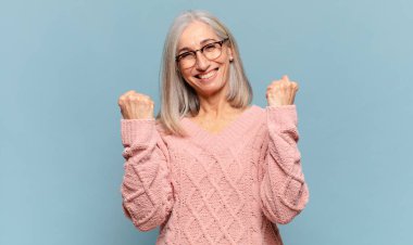 Orta yaşlı kadın zaferle bağırıyor, gülüyor, mutlu ve heyecanlı hissediyor başarıyı kutlarken.