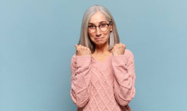 Orta yaşlı kadın kendinden emin, sinirli, güçlü ve agresif görünüyor. Yumrukları boks pozisyonunda dövüşmeye hazır.