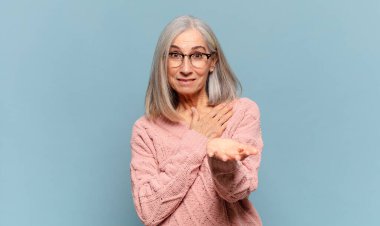 Orta yaşlı bir kadın mutlu ve aşık, bir eli kalbinin yanında gülümsüyor ve diğer eli önde uzanıyor.