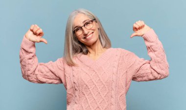 Orta yaşlı bir kadın gururlu, kibirli ve kendinden emin, tatmin olmuş ve başarılı görünüyor, kendini işaret ediyor.