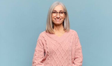 Orta yaşlı bir kadın mutlu, mutlu, kendinden emin ve rahat bir ifadeyle neşeli bir şekilde gülümsüyor.