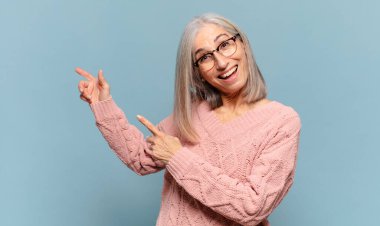 Orta yaşlı bir kadın mutlu ve şaşırmış hissediyor. Şok olmuş bir ifadeyle gülümsüyor ve bir tarafı işaret ediyor.