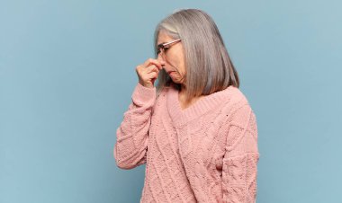 Orta yaşlı bir kadın iğrenç ve nahoş bir koku almaktan kaçınmak için burnunu tutuyor.