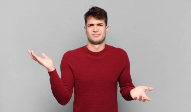 Genç adam şaşkın, şaşkın ve stresli görünüyor, farklı seçenekler arasında merak ediyor, kararsız hissediyor.