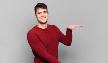 Genç adam gülümsüyor, mutlu, pozitif ve tatmin olmuş hissediyor, fotokopi alanında nesne veya konsept tutuyor veya gösteriyor