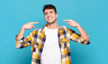 Genç adam kendinden emin bir şekilde gülümseyerek kendi geniş gülüşünü, pozitif, rahat, tatmin olmuş tavrını gösteriyor.