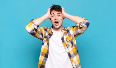 Genç adam heyecanlı ve şaşırmış görünüyor, ağzı açık, elleri başının üstünde, şanslı bir kazanan gibi hissediyor.