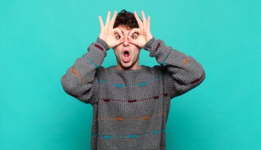 Genç adam şaşkın, şaşırmış ve şaşırmış hissediyor. Elinde şaşkın, inançsız bir bakışla gözlük tutuyor.