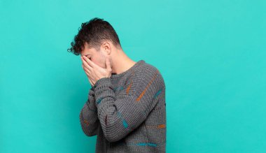 Genç adam üzgün, hayal kırıklığına uğramış bir bakışla gözlerini kapatıyor, ağlıyor, yan gözle bakıyor.