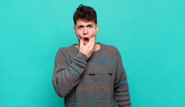 Ağzı ve gözleri açık, eli çenesinde olan genç bir adam, nahoş bir şekilde şokta, ne ya da vay canına diyor.