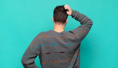 Genç adam bilgisiz ve kafası karışık, bir çözüm düşünüyor, eli kalçasında, diğeri kafasında, dikiz aynasından.