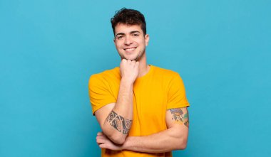 Genç adam mutlu görünüyor ve gülümsüyor. El pençe divan, merak ediyor ya da soru soruyor. Seçenekleri karşılaştırıyor.