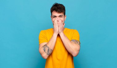 Genç adam mutlu, neşeli, şanslı ve şaşkın görünüyor. İki eliyle ağzını kapatıyor.