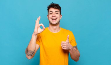 Genç adam mutlu, şaşkın, tatmin olmuş ve şaşırmış hissediyor, iyi görünüyor ve el hareketlerini gösteriyor, gülümsüyor.