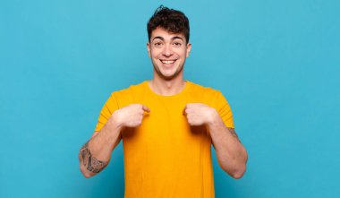 Genç adam mutlu, şaşkın ve gururlu, heyecanlı, şaşkın bakışlarla kendini işaret ediyor.