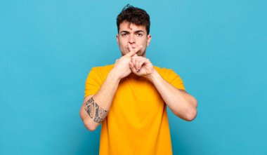 Genç adam ciddi ve hoşnutsuz görünüyor. İki parmağının önde olması reddedilerek sessizlik istiyor.