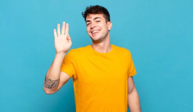 Genç adam mutlu ve neşeyle gülümsüyor, el sallıyor, seni selamlıyor ve selamlıyor, ya da hoşça kal diyor.