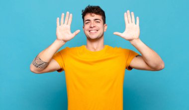 Genç adam gülümsüyor ve arkadaş canlısı görünüyor, onuncu ya da onuncu numarayı gösteriyor, eli önde, geri sayıyor.