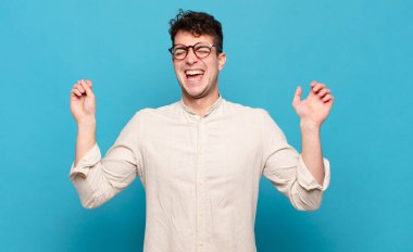 Genç adam son derece mutlu ve şaşırmış görünüyor, başarıyı kutluyor, bağırıyor ve zıplıyor.