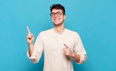 Genç adam mutlu bir şekilde gülümsüyor ve her iki elinle de fotokopi uzayında nesne gösteriyor.