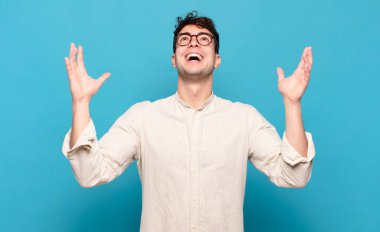 Genç adam mutlu, şaşkın, şanslı ve şaşırmış hissediyor, zaferi kutluyor, iki eli havada.