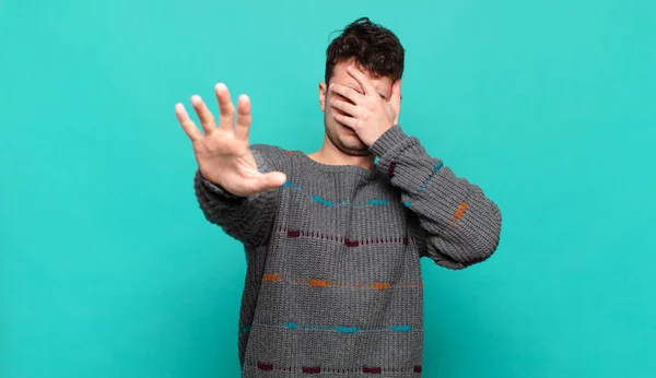 young man covering face with hand and putting other hand up front to stop camera, refusing photos or pictures