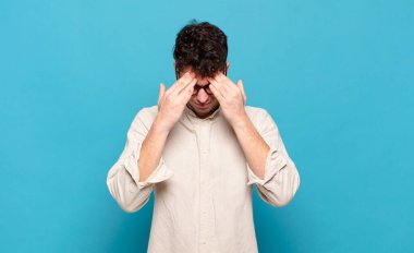 Genç adam stresli ve hayal kırıklığına uğramış görünüyor, baskı altında çalışıyor, başı ağrıyor ve sorunlarla boğuşuyor.