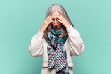 Stresli ve hayal kırıklığına uğramış görünen orta yaşlı bir kadın, baskı altında çalışıyor, başı ağrıyor ve sorunları var.