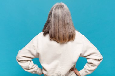 Orta yaşlı bir kadın kafası karışık ya da dolgun ya da şüphe ve soru dolu, merak ediyor, elleri kalçasında, dikiz aynasından.