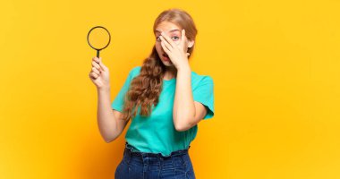 Şok olmuş, korkmuş ya da korkmuş görünüyor, yüzleri elle kaplıyor ve parmaklarının arasına bakıyor.