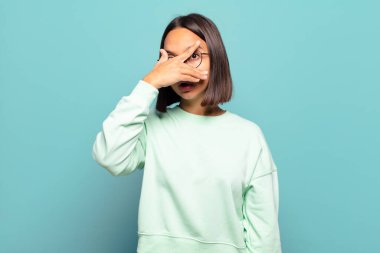 Genç İspanyol kadın şok olmuş, korkmuş ya da korkmuş görünüyor. Yüzü elle kaplanmış ve parmaklarının arasından gizlice bakıyor.