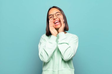 Genç İspanyol kadın mutlu, heyecanlı ve pozitif hissediyor. Elleri ağızda, bağırarak bağırıyor.