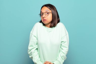 Genç İspanyol kadın omuz silkiyor, kafası karışık ve emin değil, kolları bağlı ve şaşkın görünüyor.