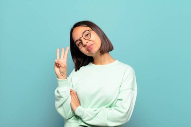 Genç İspanyol kadın gülümsüyor ve arkadaş canlısı görünüyor. Üç ya da üç numarayı gösteriyor. Elleri önde, geri sayıyor.