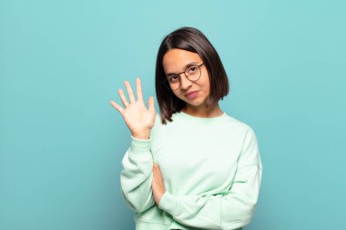 Genç İspanyol kadın gülümsüyor ve arkadaş canlısı görünüyor, 5 ya da 5 numarayı gösteriyor, elleri önde, geriye doğru sayıyor