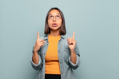 Genç İspanyol kadın şaşkınlık içinde ve ağzı açık. Şok olmuş ve şaşırmış bir bakışla yukarı bakıyor.