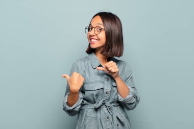 Genç İspanyol kadın neşeli bir şekilde gülümsüyor ve yan taraftaki fotokopi alanını gösteriyor, mutlu ve tatmin olmuş hissediyor.