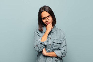 Genç İspanyol kadın ciddi, düşünceli ve güvensiz görünüyor, bir kolu çapraz ve çene üzerinde, seçenekleri tartıyor