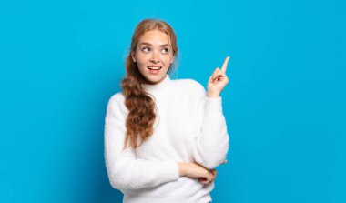 Sarışın, güzel bir kadın mutlu bir şekilde gülümsüyor ve yan bakıyor, merak ediyor, düşünüyor ya da bir fikri var.