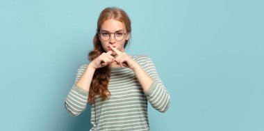 Sarışın, güzel bir kadın. Ciddi ve hoşnutsuz görünüyor. İki parmağın önde olsun, reddedilmek üzere, sessizlik istiyor.