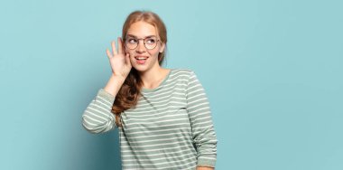 Sarışın, güzel bir kadın gülümsüyor, tuhaf bir şekilde yan tarafa bakıyor, dedikoduları dinlemeye ya da bir sırrı duymaya çalışıyor.