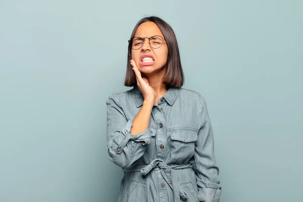 頬を抱え痛みを伴う歯痛を抱える若いヒスパニック系の女性病気悲惨で不幸な歯医者を探しています — ストック写真