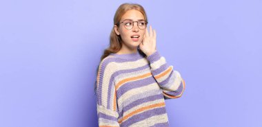 Sarışın, güzel bir kadın ciddi ve meraklı görünüyor, dinliyor, gizli bir konuşma ya da dedikodu duymaya çalışıyor, kulak misafiri oluyor.