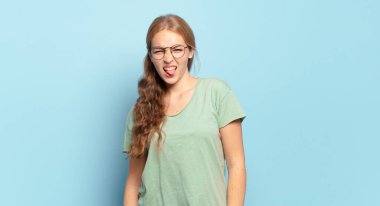 Sarışın, güzel bir kadın tiksinmiş ve rahatsız olmuş hissediyor, dilini dışarı çıkarıyor, iğrenç ve iğrenç bir şeyden hoşlanmıyor.