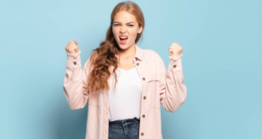 Sarışın, güzel bir kadın sinirli bir ifadeyle bağırıyor ya da yumruklarıyla başarıyı kutluyor.