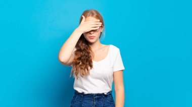 Sarışın, güzel bir kadın tek eliyle gözlerini kapatıyor. Korkmuş ya da endişeli, merak ediyor ya da körü körüne bir sürpriz bekliyor.