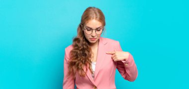 Sarışın, güzel bir kadın neşeli ve sıradan bir şekilde gülümsüyor, aşağıya bakıyor ve göğsüne işaret ediyor.