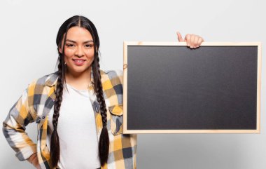 İspanyol kadın mutlu bir şekilde gülümsüyor, eli kalçasında ve kendinden emin, olumlu, gururlu ve arkadaş canlısı bir tavırla.