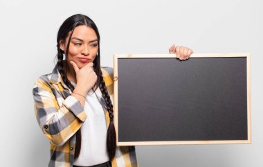 İspanyol kadın mutlu, kendinden emin bir ifadeyle gülümsüyor, çenesinde elleri, merak ediyor ve yan tarafa bakıyor.